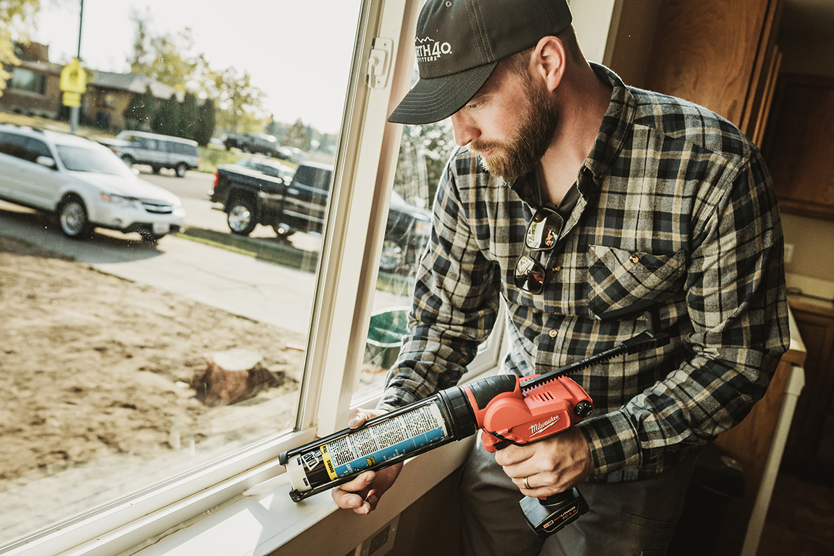A man using caulk on the inside of his windows