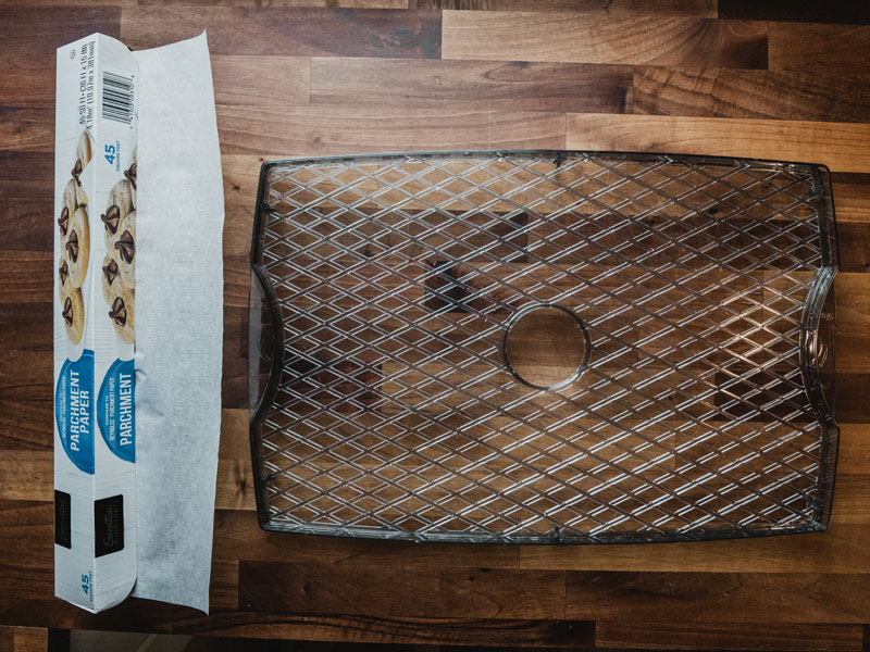 Parchment and Craftworx tray A roll of parchment paper sits next to a Craftworx dehydrator tray on a clean butcher block