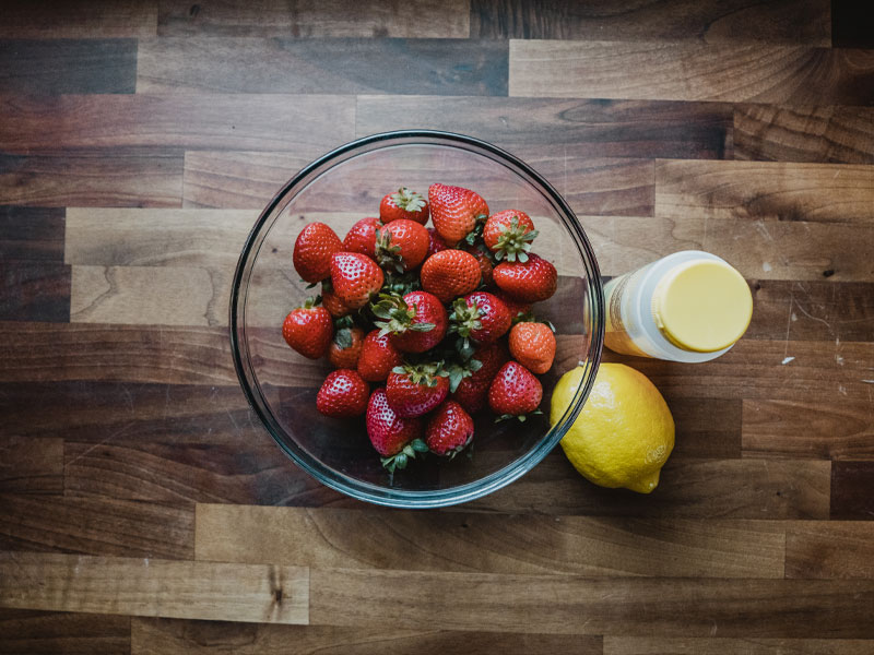 Fruit leather ingredients Fresh Florida strawberries in a clear glass bowl sit next to a lemon and a jar of Smoot honey on a butcher block
